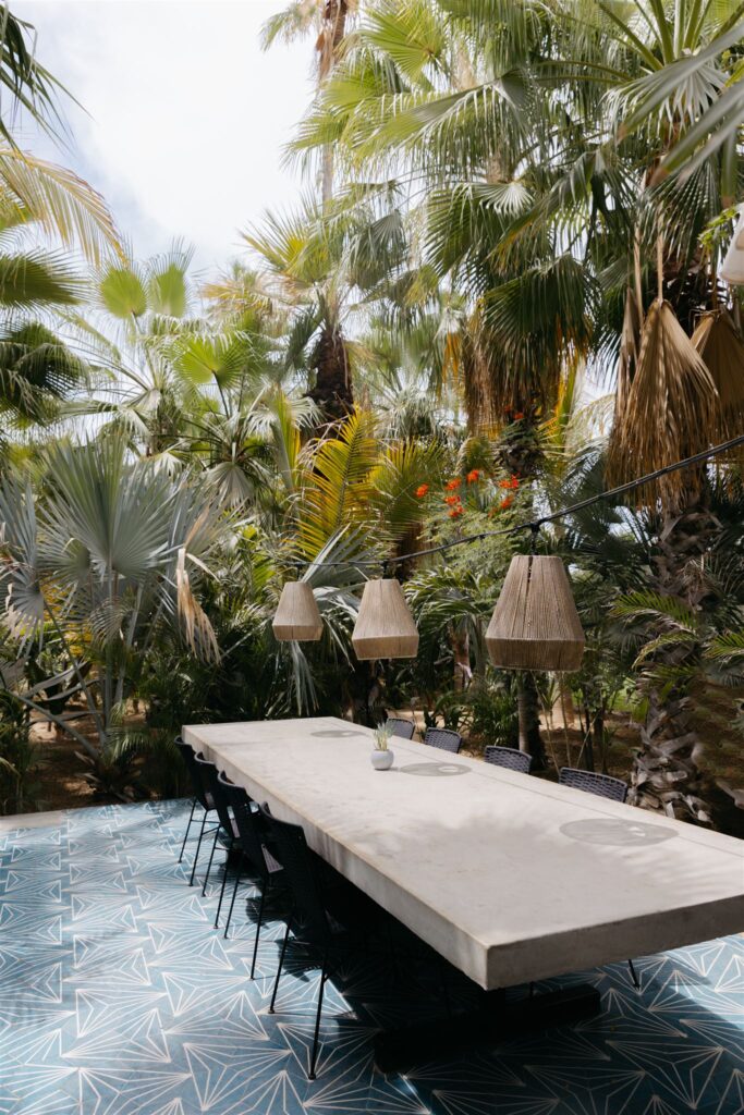 long concrete table with basket lamp shades hanging in the middle of a jungle with palm trees