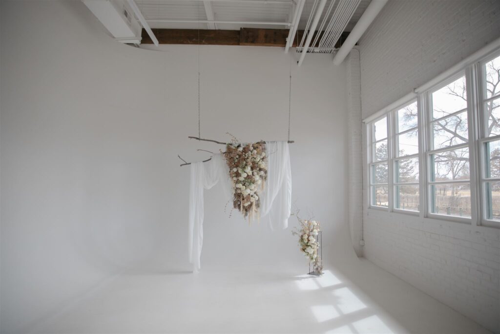 bright natural light photography studio with large floral installation hanging from high beamed ceilings