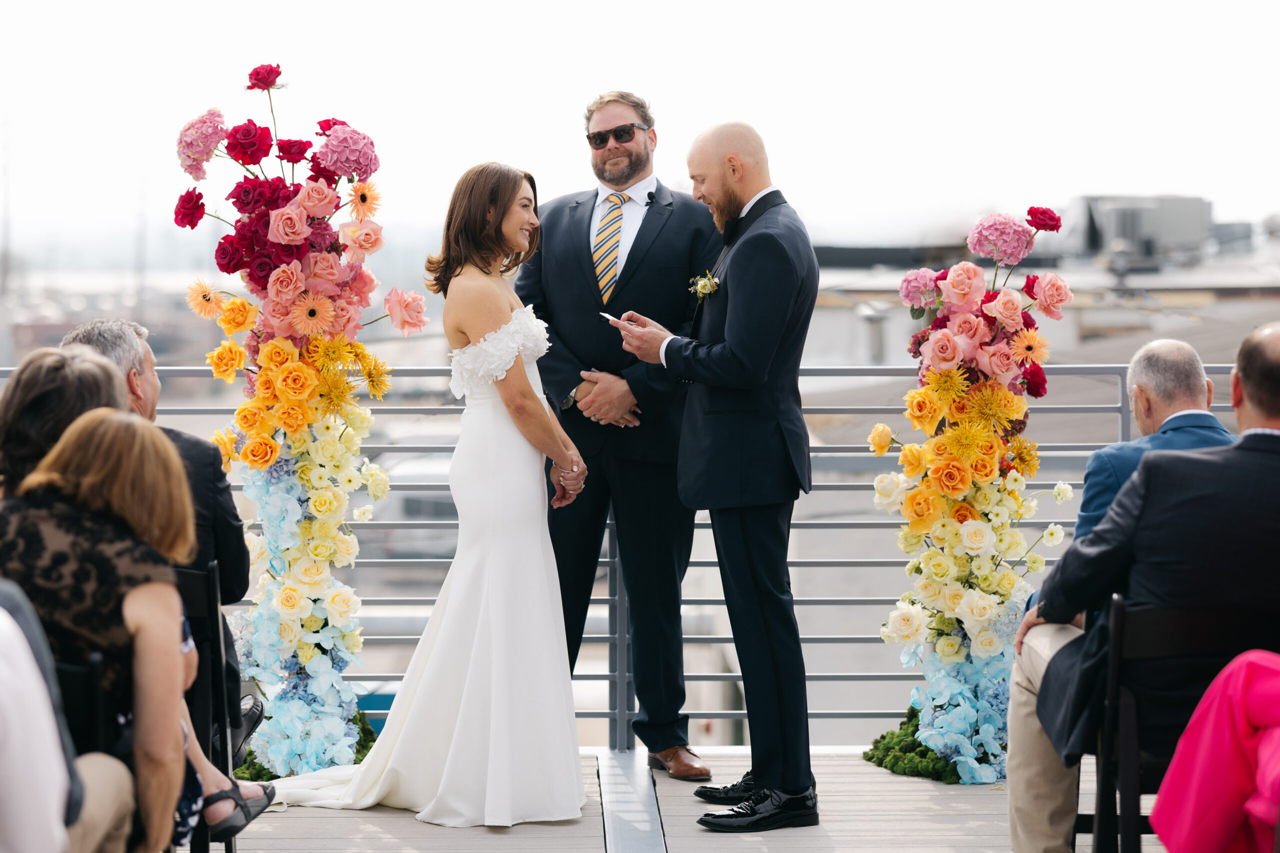 Bride and groom standing between colorful flower arch reading vows on rooftop patio at denver wedding venues