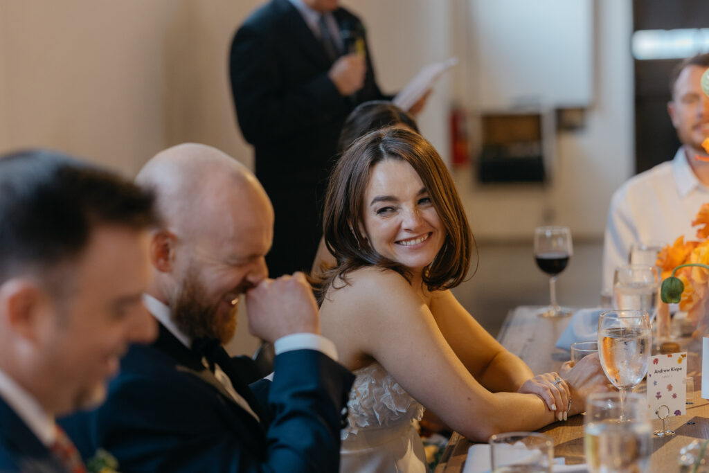 bride laughing with groom during wedding toasts 