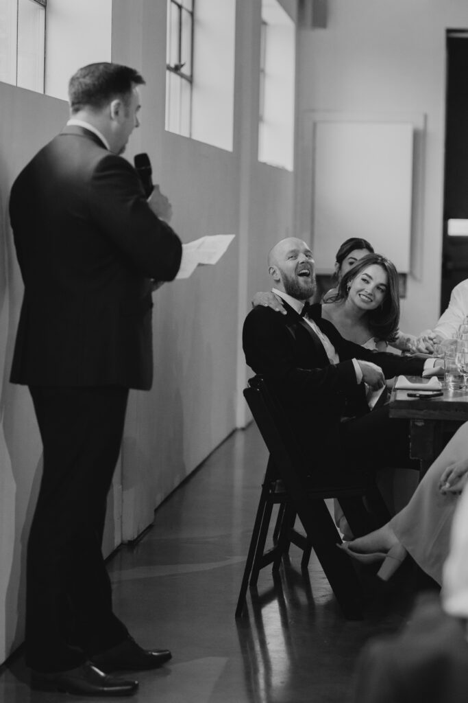 black and white image of groom listening to speeches during reception