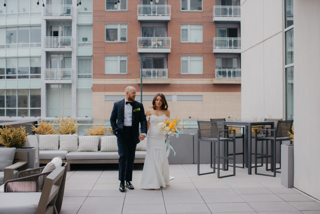 bride and groom walking towards frame smiling with city buildings in backdrop