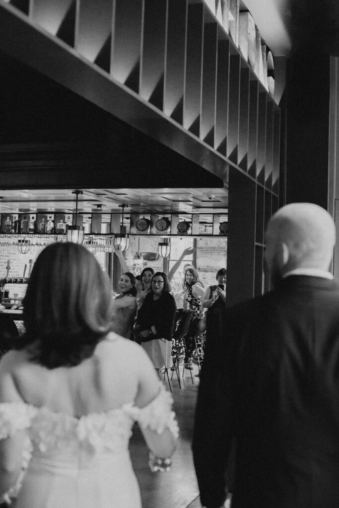 bride and groom walking into downtown bar facing away from camera being greeted by families