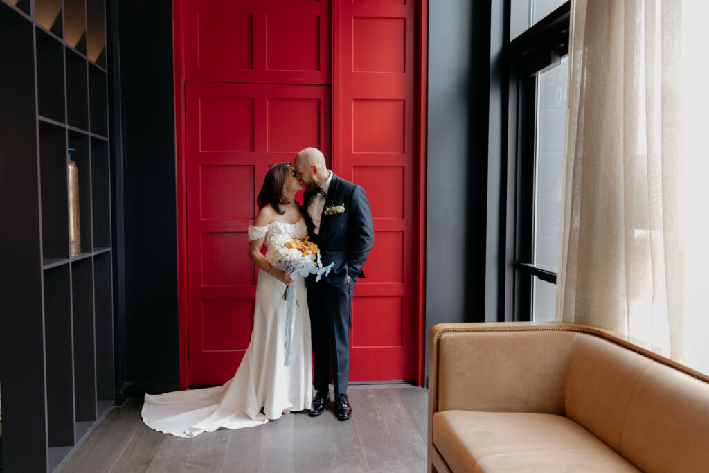 bride and groom standing in front of red doors kissing