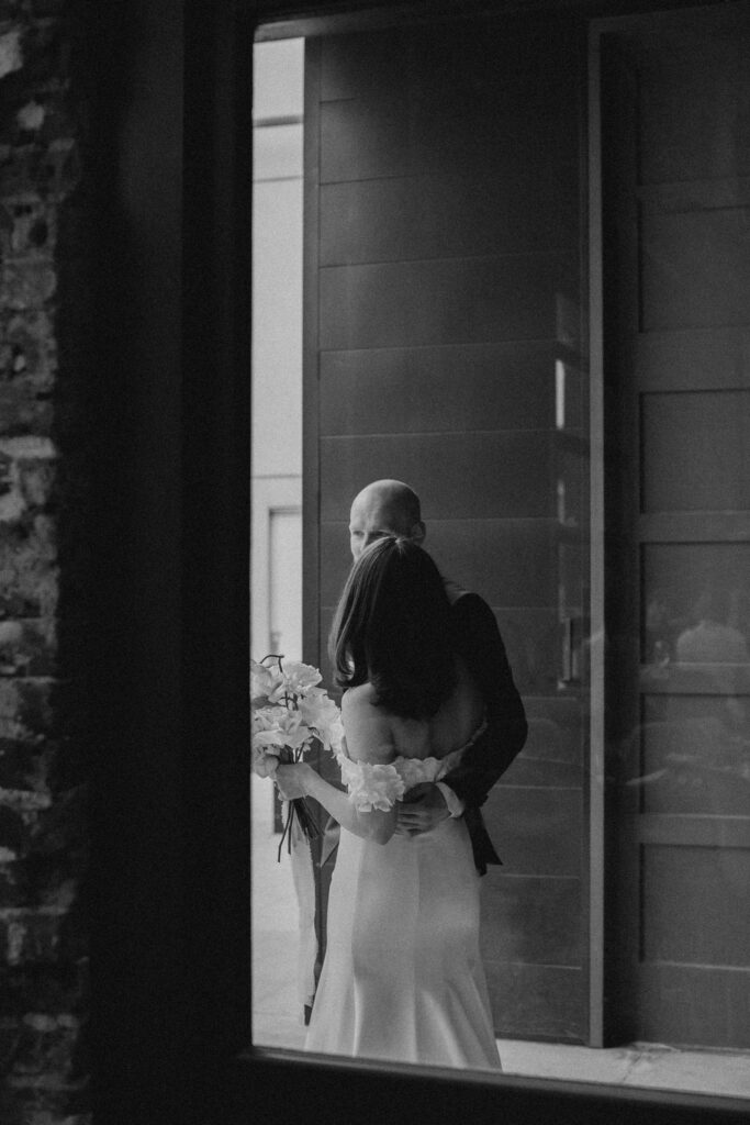 black and white image of bride and groom standing outside a glass window