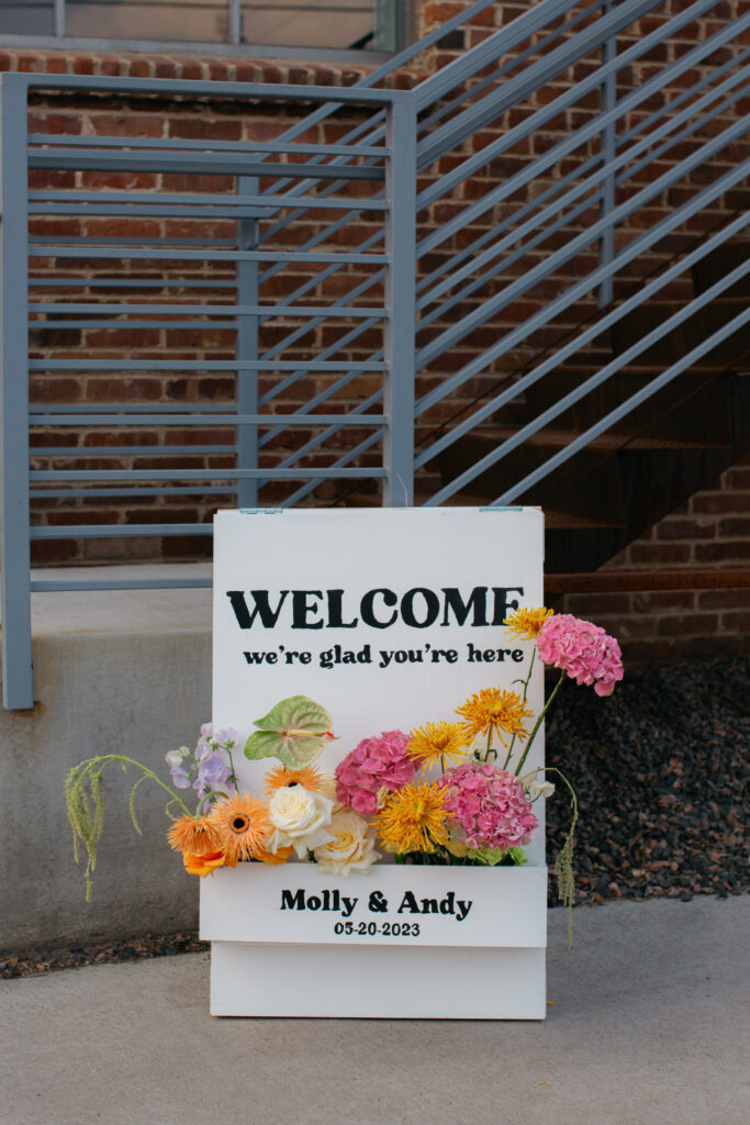 wedding welcome sign filled with flowers sitting out front of industrial wedding venue