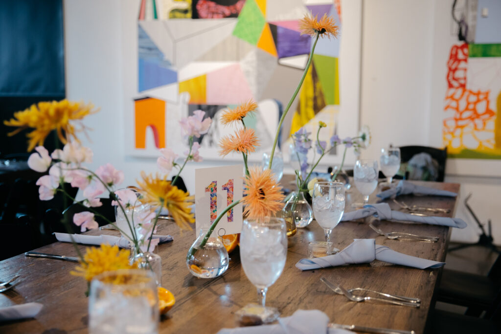 orange floral center pieces on wood tables with art filled walls in background