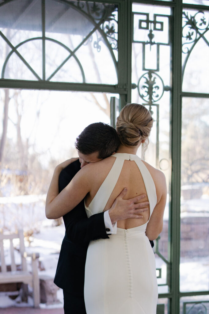 Groom hugs bride while standing inside Woodlands Mosaic Solarium at Botanic Gardens with Denver wedding photographer