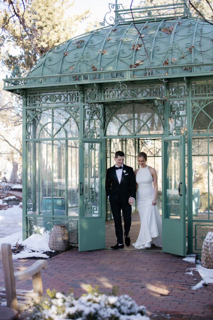 Bride and groom exit glass doors of Woodlands Mosaic Solarium during Denver wedding photos