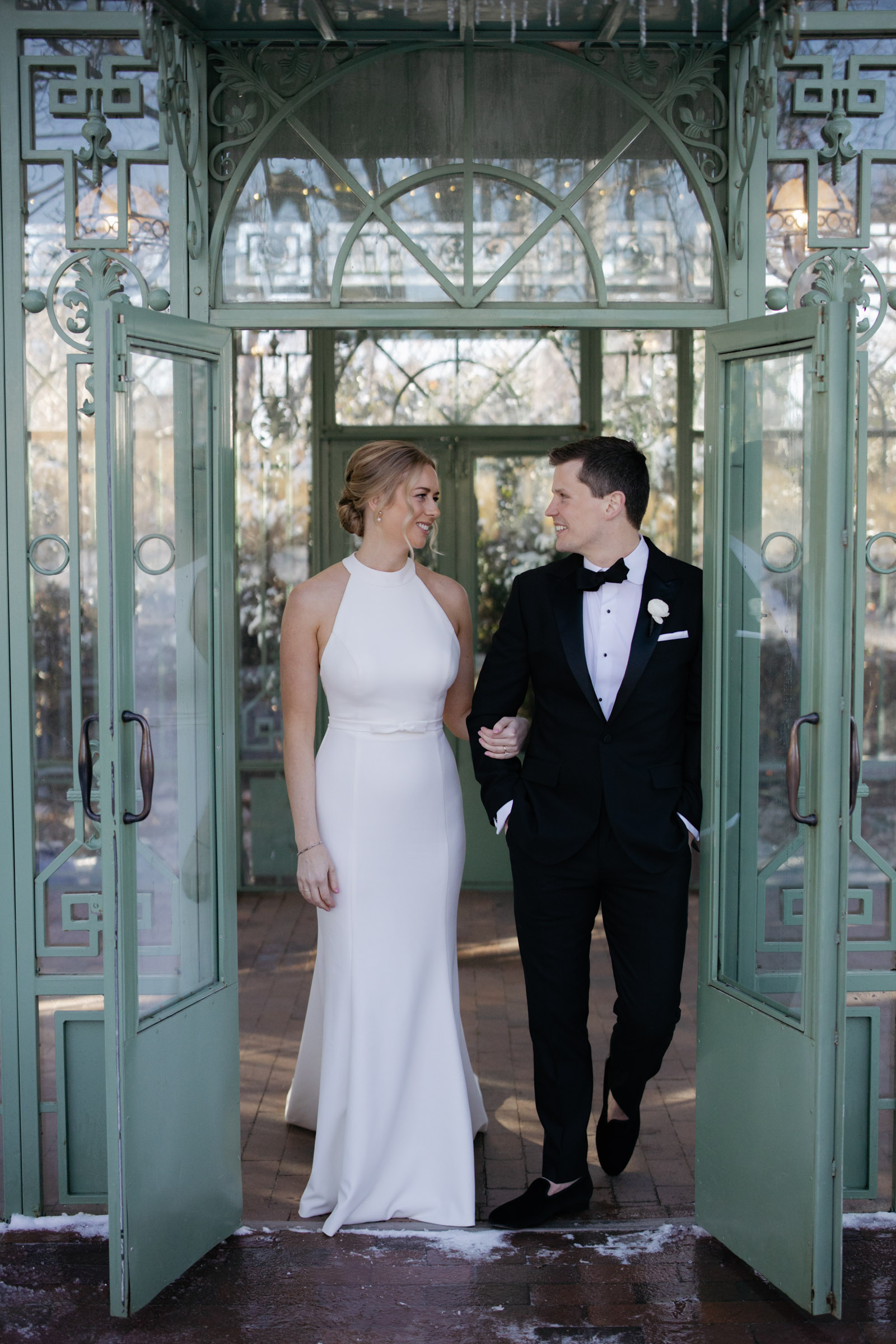 Bride and groom standing in glass doors of Woodlands Mosaic Solarium during Denver wedding photos