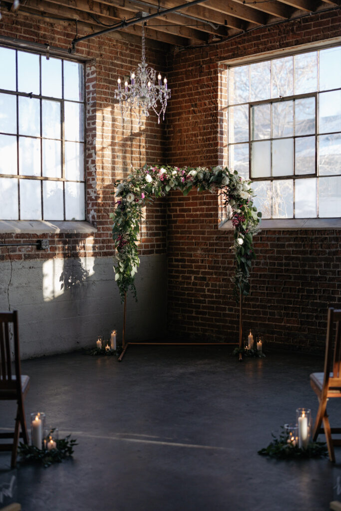 Floral arch backdrop set up for Denver wedding at Moss, set along brick walls and industrial windows
