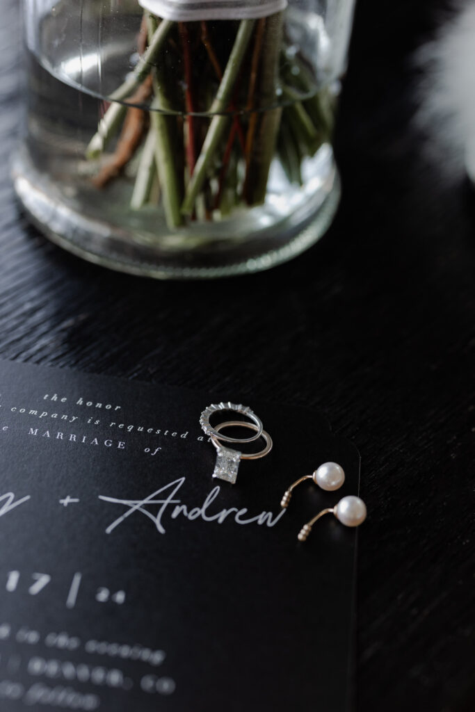 Diamond ring and earrings sit on modern, Denver wedding invitation