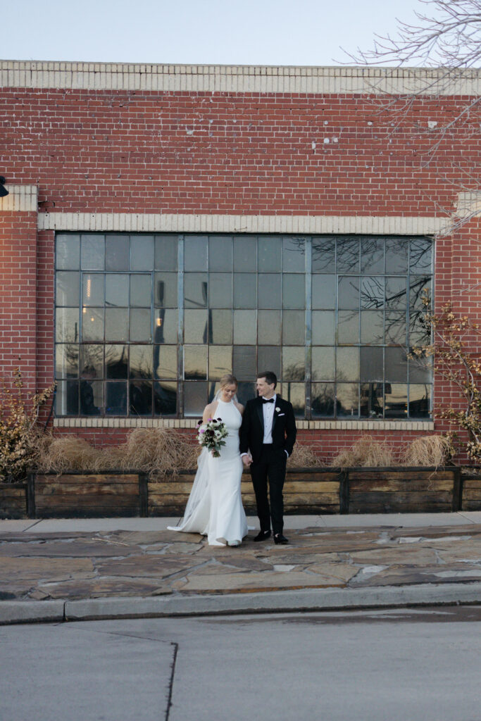Newlyweds walking on stone pathway in front of Moss, Denver wedding venue
