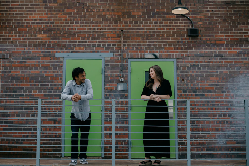 Couple standing in front of green double doors and brick wall during Denver couples photography session