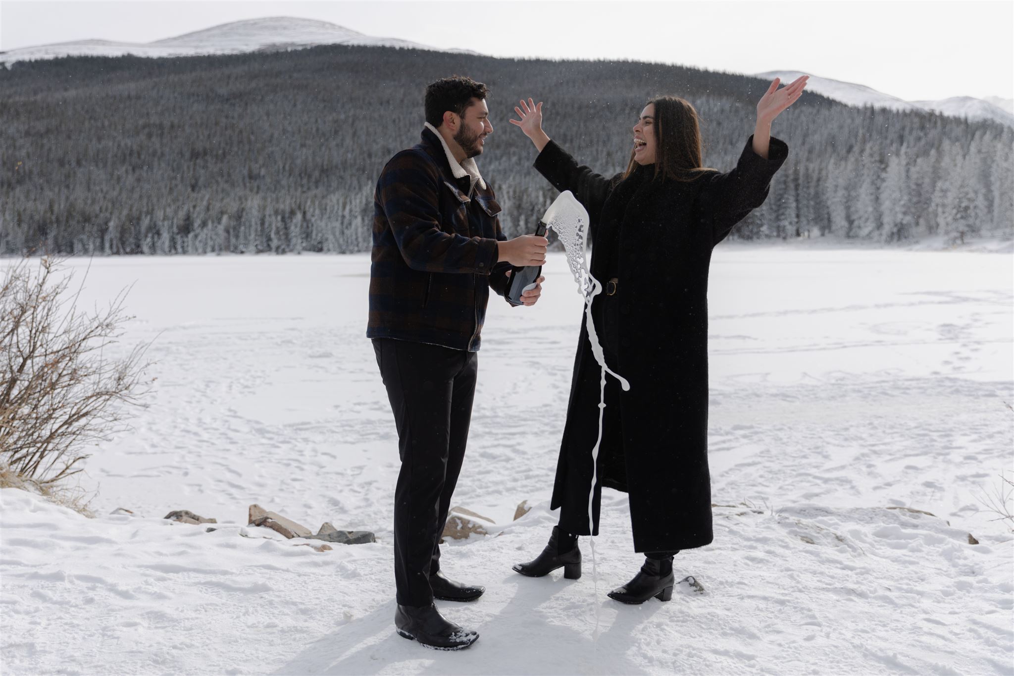 Couple holding exploding champagne bottle during Colorado engagement photos at Echo Lake