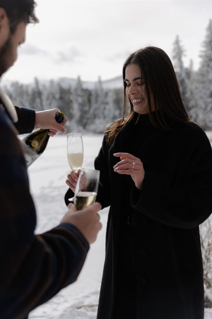 Couple pouring champagne during Colorado engagement photos of winter engagement photos session