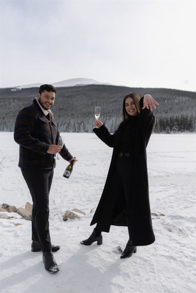 Couple smiling holding glasses of champagne showing off engagement ring during Colorado engagement photos