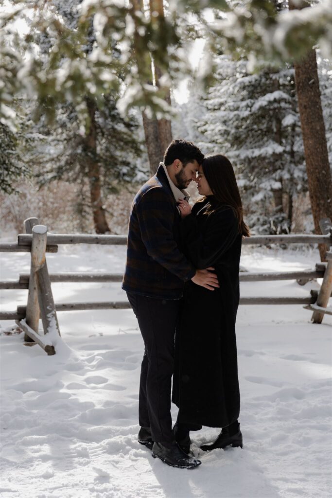 Couple embracing one another under snowy covered trees during Colorado engagement photos taken by Colorado engagement photographer Caroline Brackney