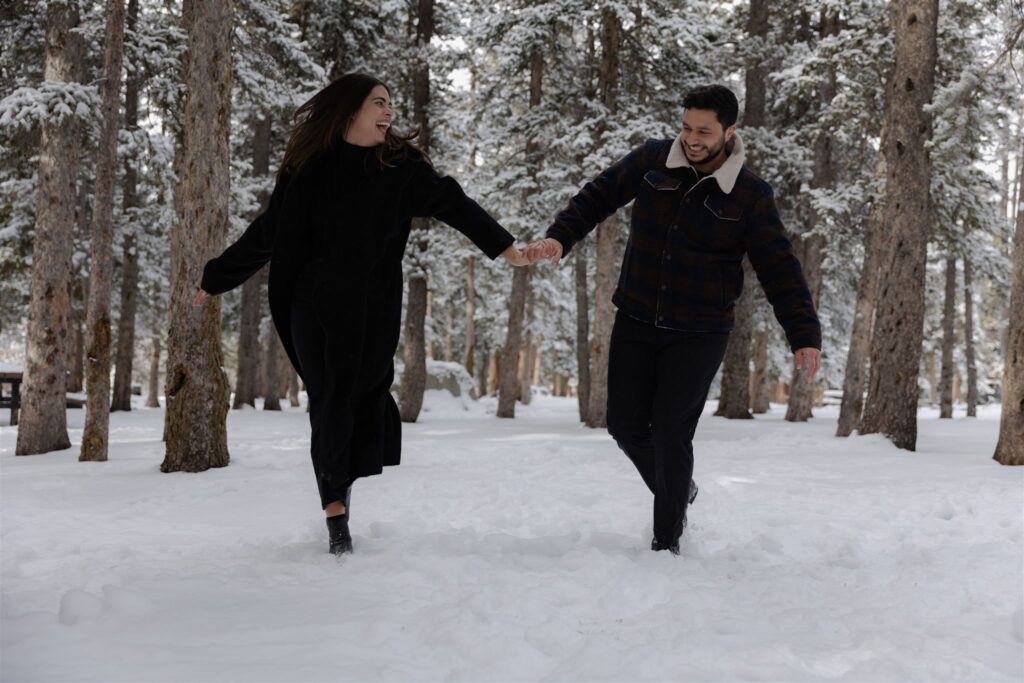 Couple running while holding hands in snowy forest during engagement photos in Colorado at Echo Lake Park, top Colorado engagement photo locations
