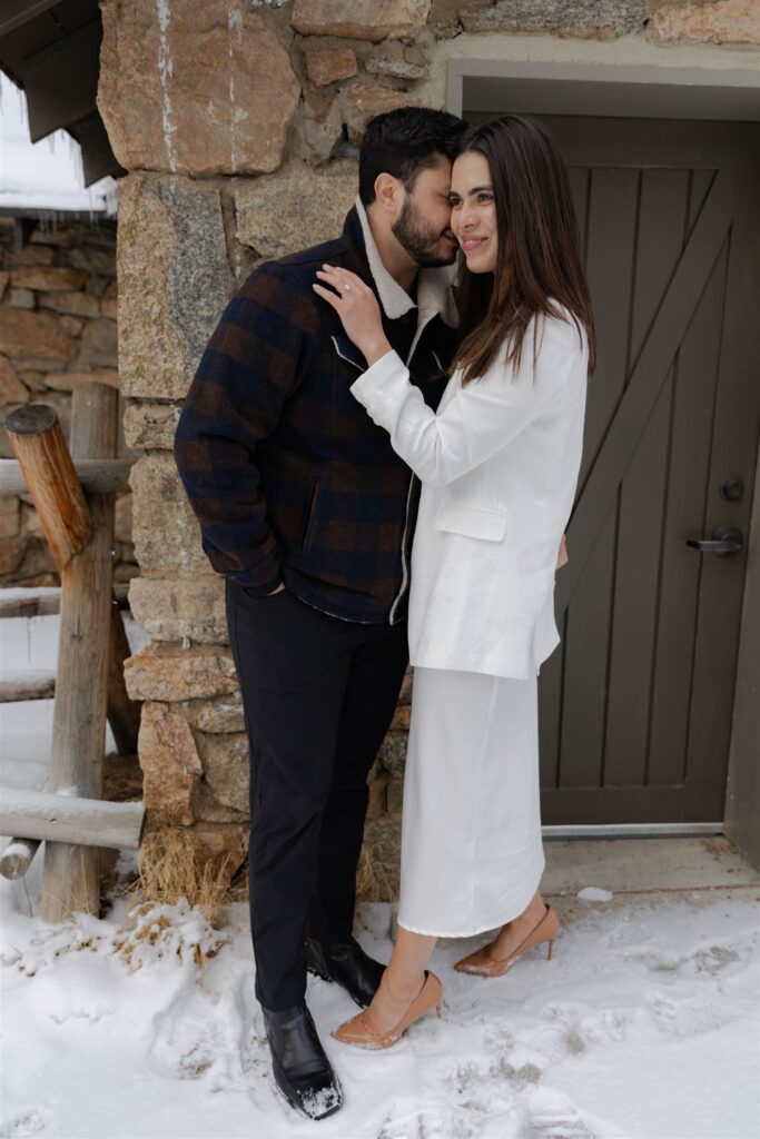 Couple standing in front of outdoor building looking off into distance during Colorado engagement photos for winter engagement picture ideas