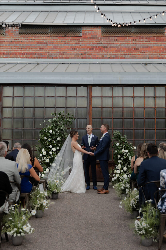 bride and groom standing in front of large industrial glass doors during wedding ceremony