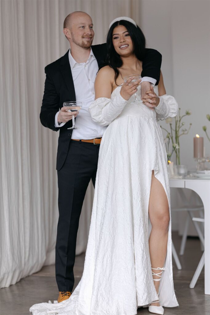 Couple standing in front of modern, white backdrop with intimate table setup during elopement photos at Realm studio