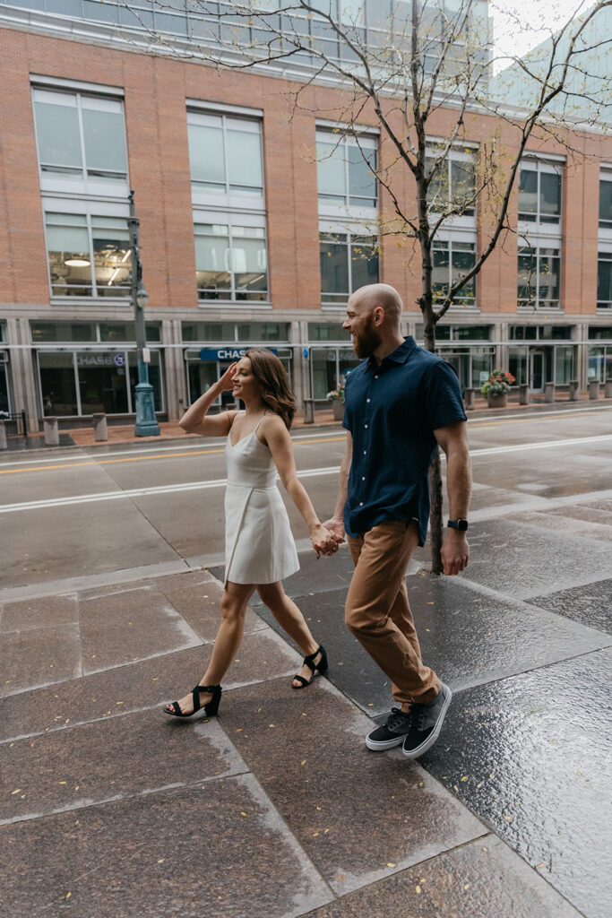 Couple walking streets of Downtown Denver, exploring places to take engagement photos