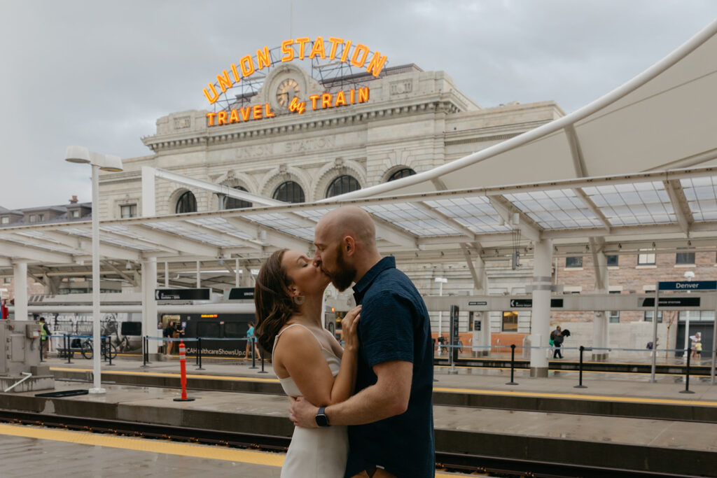 couple kissing in front of train station kissing with Denver Union Station in background