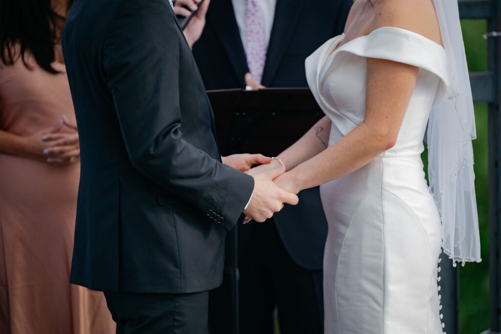 up-close view of groom holding bride's hands during wedding ceremony while standing on bridge at Coohills restaurant in downtown Denver