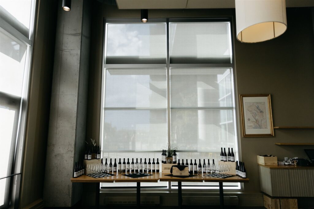 a table filled with wine bottles and wine glasses, set in front of a glass window and concrete walls in Coohills Restaurant of Downtown Denver