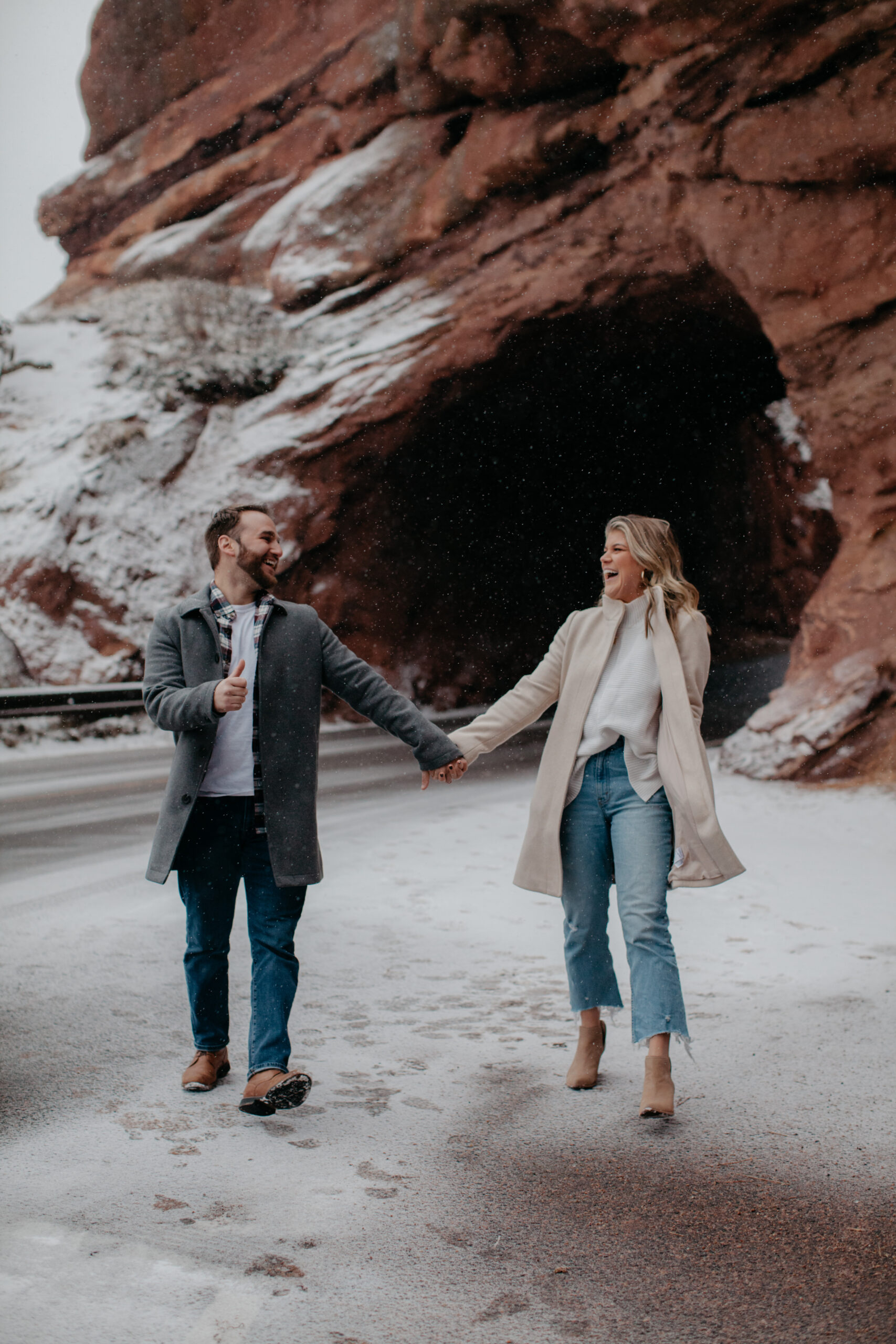 Couple holding hands laughing with Red Rocks tunnel in background
