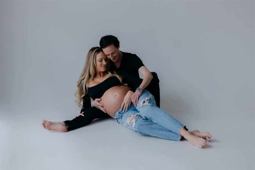 couple sitting on floor of white, natural light photo studio for maternity photos