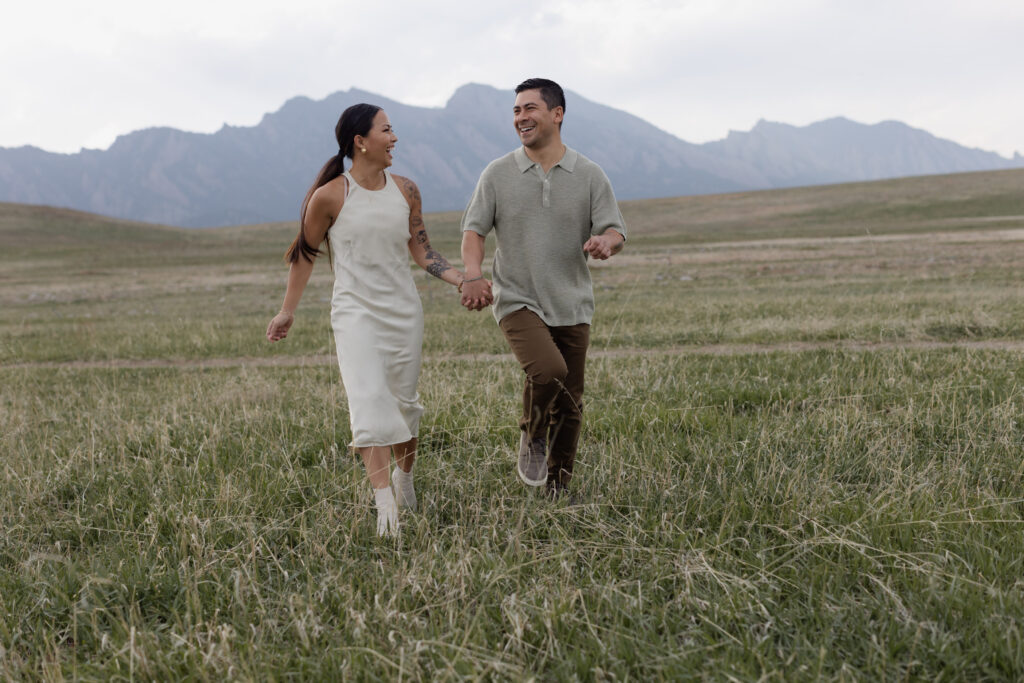 Couple running through field with Boulder flatirons in backdrop during engagement session