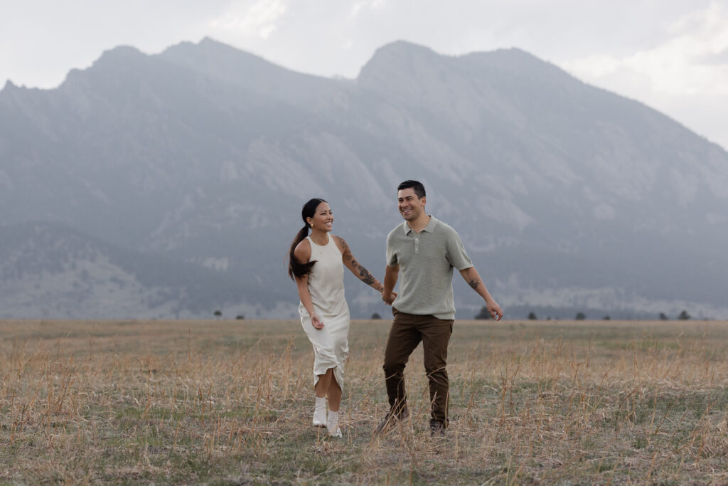 Couple holding hands in front of Boulder Flatirons engagement session