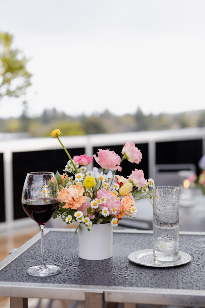 Wine and colorful flowers sit on table during rooftop wedding welcome party