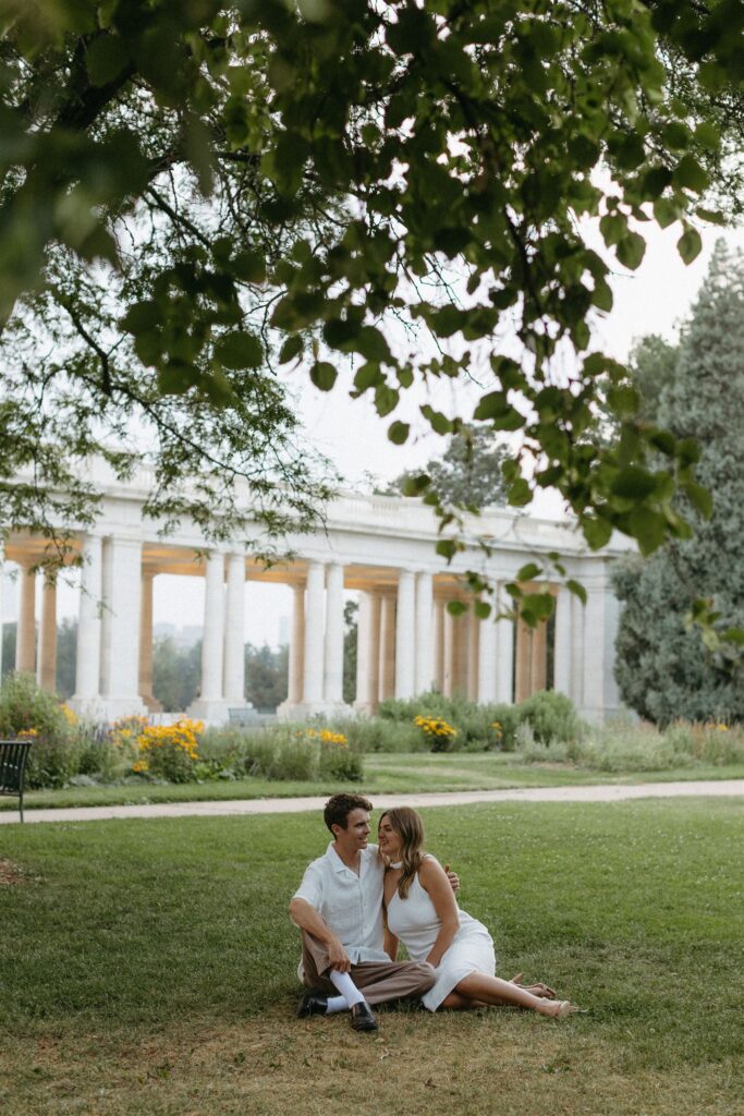 couple sitting under trees during Denver engagement session at Cheesman Park