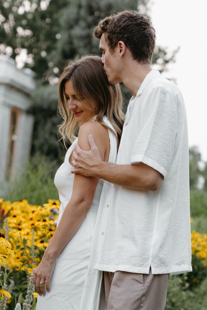 couple kissing in row of flowers at Cheesman Park during Denver engagement photos