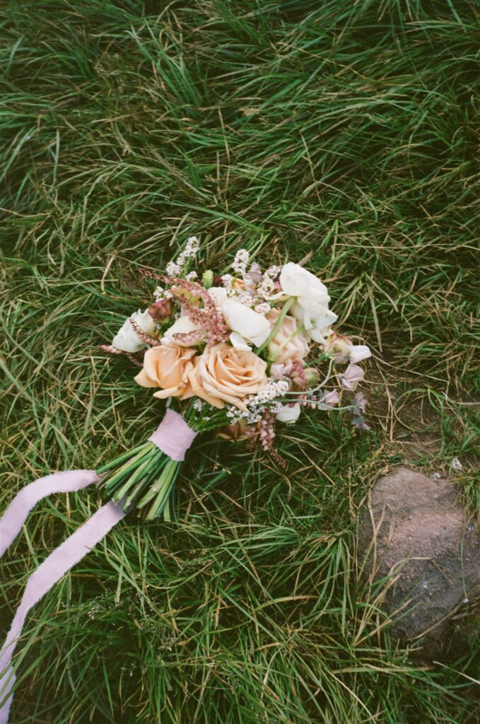 Film scan photo with wedding florals sit on grass during elopement at Piney River Ranch