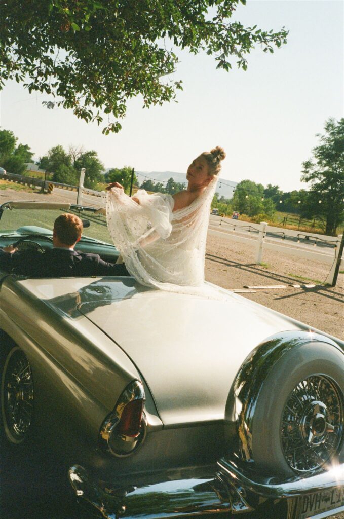 Bride sits on hood of classic car during Colorado wedding photography on film