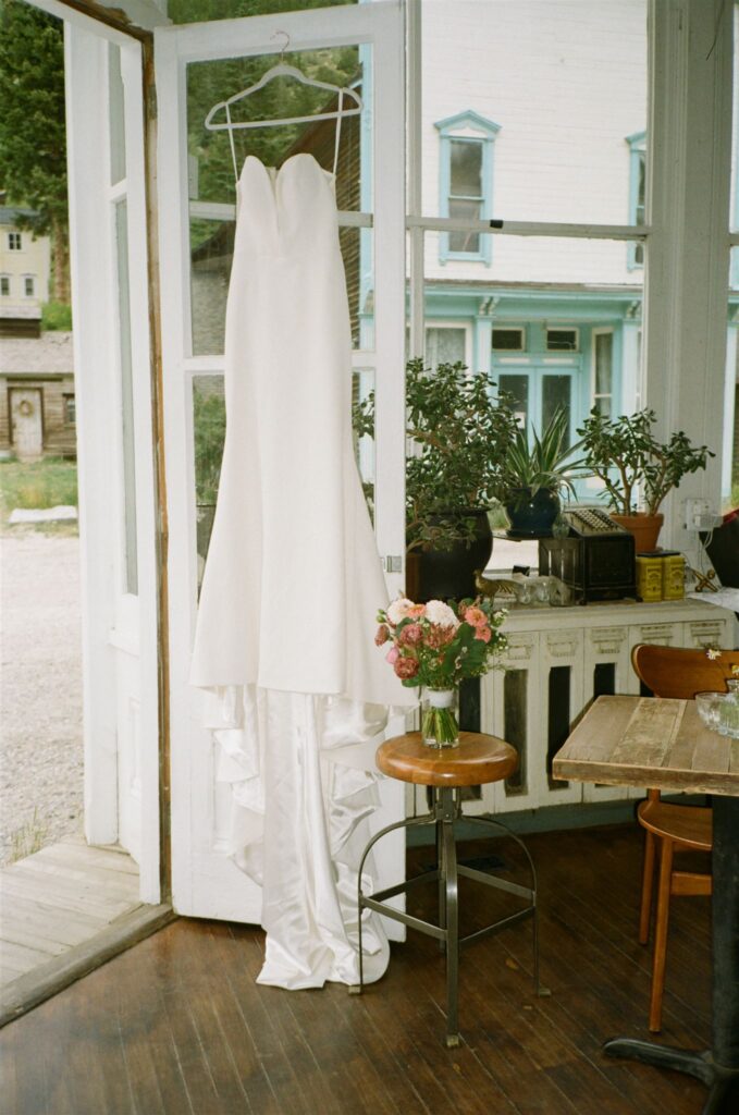 Bride's dress hangs from door of Silver Plume Bread Bar during Colorado elopement wedding photography on film